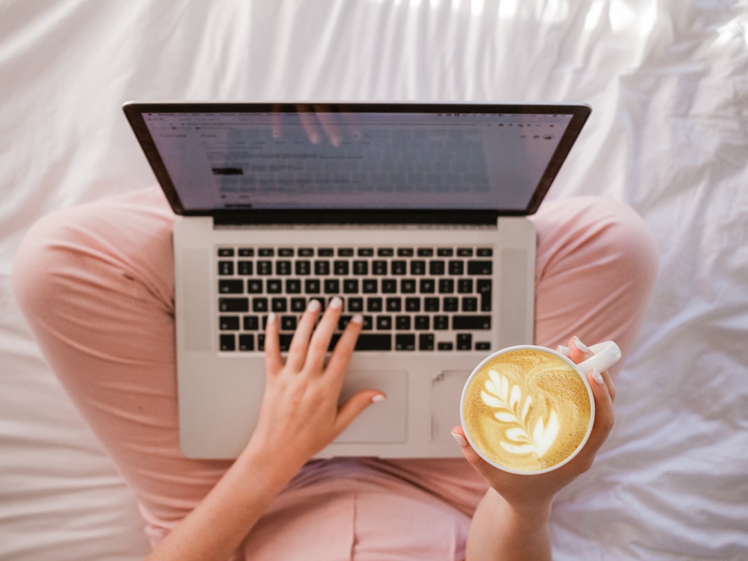 A woman using a laptop while holding a cup of coffee.